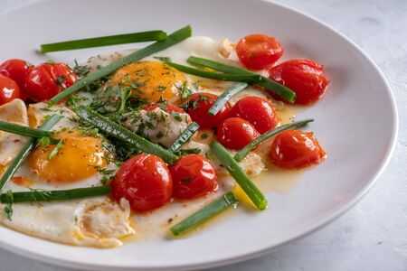 Fried eggs with cherry tomatoes and green onions on a white plate with white fried breadの写真素材
