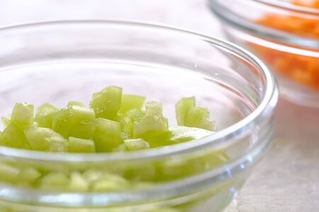 finely chopped green bell peppers and carrots in a glass cup on a gray background close-upの写真素材
