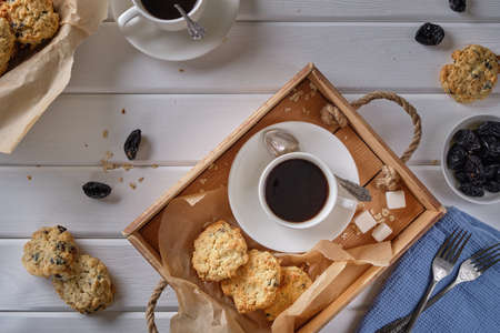 Cup of black coffee and oatmeal cookies with prunes on a wooden tray on a white wooden tableの写真素材