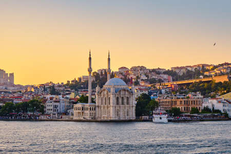 Ortakoy wharf on the Bosphorus, view of the mosque in the background of the city at sunset. Ferries stand on the wharf, people walk on the pierの写真素材