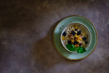 Buckwheat porridge with walnut, raisins and prunes on a green plate on a brown background under concrete. Delicious and healthyの写真素材