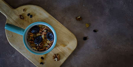 Dry fruits in a cup on a cutting board on a dark background close-up. Walnut, yellow raisins and...
