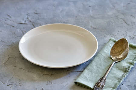 White plate, spoon and napkin for serving the table on gray concrete background close-up