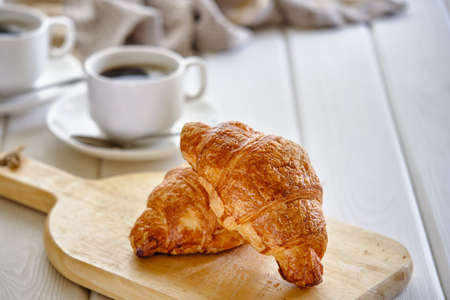 A crispy croissant with almond filling and hot black coffee on a wooden board on a light concrete table. Tasty breakfastの写真素材
