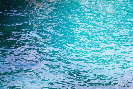 Tranquil sparkling azure blue sea water texture with surface ripples and underwater rocks in a full...