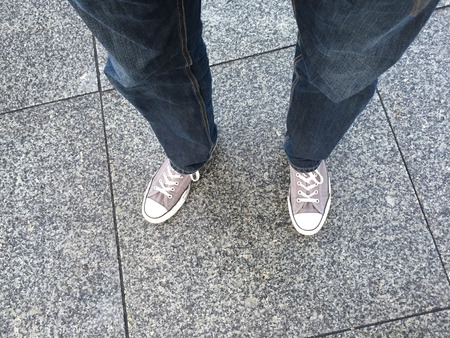 Wide angle view of the legs and feet of a person wearing jeans and sneakers from a first person...