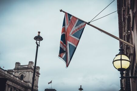 Union jack flag on pole under lamp near old building under cloudy gray overcast skyの写真素材