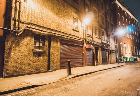 Empty background of wide urban alley at night with lamps and large garage door on brick buildingの写真素材