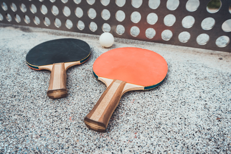 Two wooden ping pong bats and ball on an outdoor table with a perforated metal net conceptual of sport and an active lifestyleの写真素材