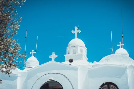 White greek orthodox church with crosses on domed cupolas against a clear sunny blue sky, low angle view of the rooftopの写真素材
