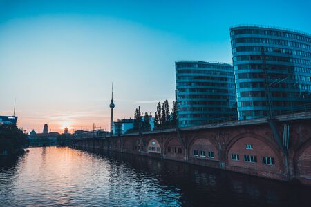 Low angle view of waterfront apartments along a placid river with a setting sun in the distanceの写真素材