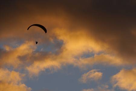 Silhouette of a paraglider against sunset lit orange cloudsの写真素材