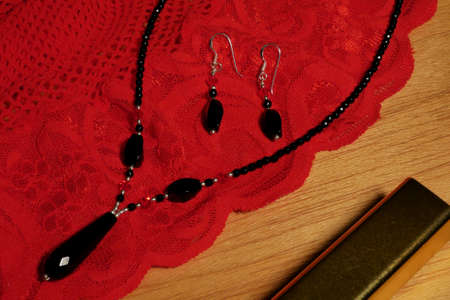 Black onyx and siver jewellery laid on red lace with a lipstick case.の写真素材