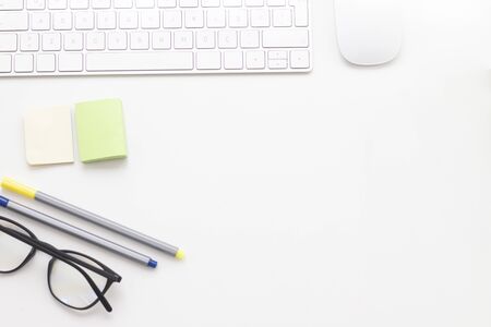 Working white desk with pencil, pen, glasses, keyboard, mouse and stickerの写真素材
