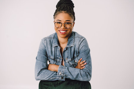 Young attractive African American woman in green dress with jean jacket and smiling in gray...