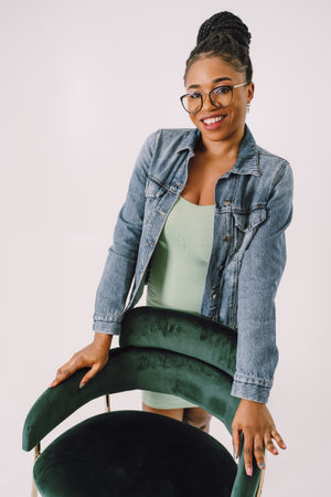 Young attractive African American woman in green dress with jean jacket and smiling in gray backgroundの写真素材