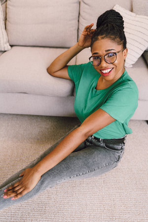 Attractive black woman sitting on the floor and holding sofa smiling. Home conceptの写真素材