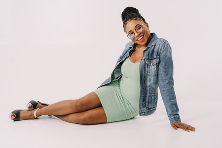Young attractive African American woman in green dress with jean jacket and smiling in gray backgroundの写真素材