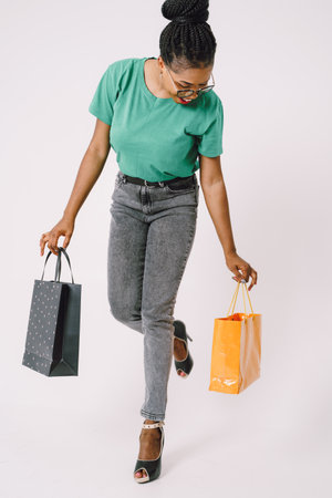 Beautiful young African American woman with shopping bags in green shirt and in gray backgroundの写真素材