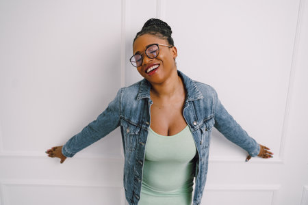 Young attractive African American woman in green dress with jean jacket and smiling in gray backgroundの写真素材