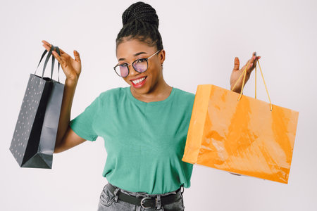 Beautiful young African American woman with shopping bags in green shirt and in gray backgroundの写真素材