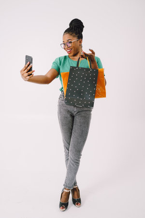 Beautiful young African American woman with shopping bags in green shirt and in gray backgroundの写真素材