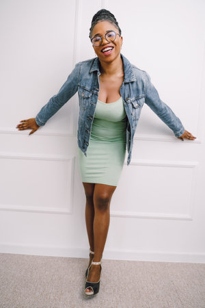 Young attractive African American woman in green dress with jean jacket and smiling in gray backgroundの写真素材