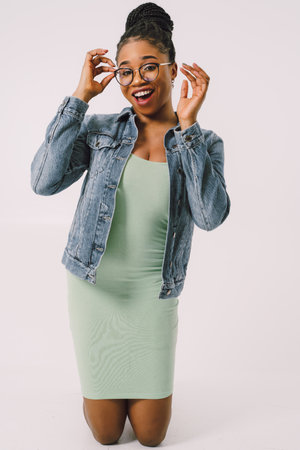 Young attractive African American woman in green dress with jean jacket and smiling in gray backgroundの写真素材