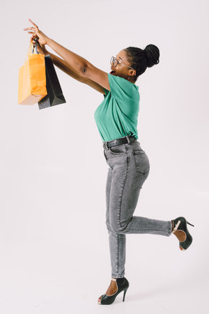 Beautiful young African American woman with shopping bags in green shirt and in gray backgroundの写真素材