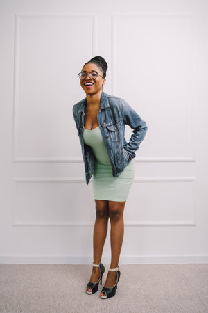 Young attractive African American woman in green dress with jean jacket and smiling in gray backgroundの写真素材
