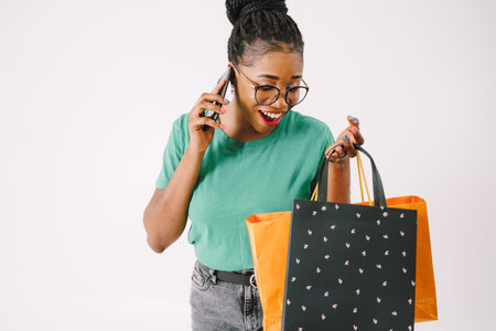 Happy black woman taking selfie with colorful shopping bags and looking down in gray background