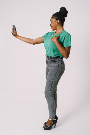 Attractive young African American woman smiling and holding smartphone in gray backgroundの写真素材
