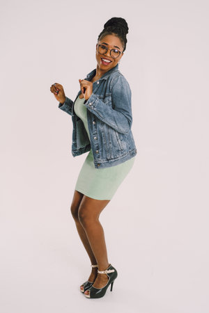 Young attractive African American woman in green dress with jean jacket and smiling in gray backgroundの写真素材