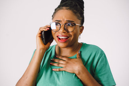 Attractive young African American woman smiling and holding smartphone in gray backgroundの写真素材