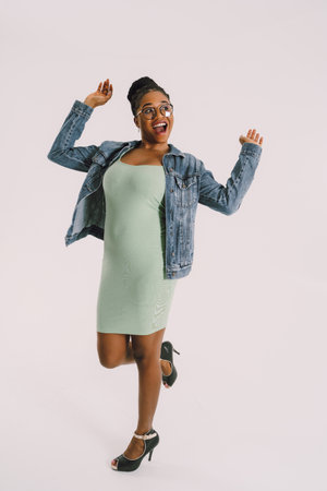 Young attractive African American woman in green dress with jean jacket and smiling in gray backgroundの写真素材