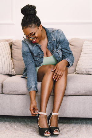 Beautiful young African American woman sitting on sofa and smiling in living roomの写真素材