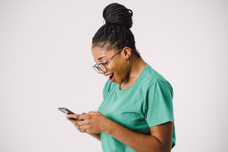 Attractive young African American woman smiling and holding smartphone in gray backgroundの写真素材