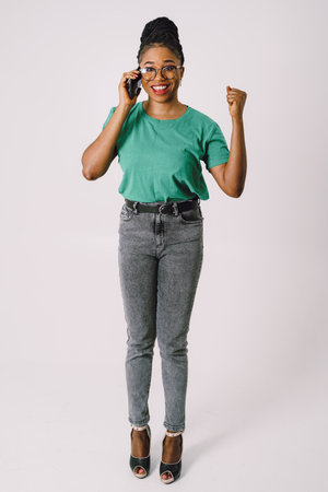 Attractive young African American woman smiling and holding smartphone in gray backgroundの写真素材
