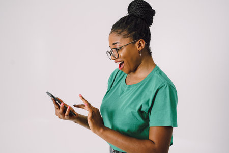 Attractive young African American woman smiling and holding smartphone in gray backgroundの写真素材