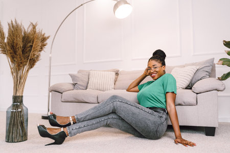 Attractive black woman sitting on the floor and holding sofa smiling. Home conceptの写真素材