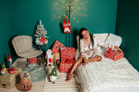 Young happy African American woman in a dress smiling on bed and playing with Christmas decorationの写真素材