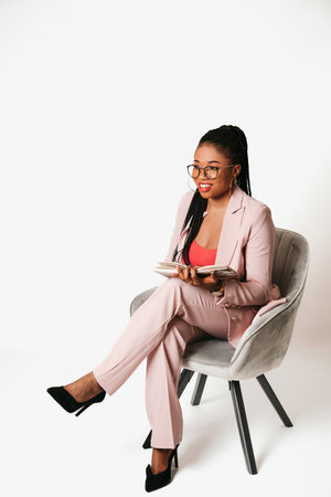 Cheerful young black woman sitting and smiling on white background with bookの写真素材