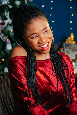 Portrait of happy young black woman in red dress on Christmas decorated backgroundの写真素材