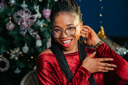 Portrait of happy young black woman in red dress on Christmas decorated backgroundの写真素材