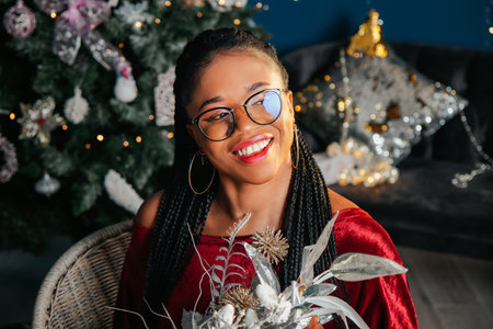 Young beautiful African American woman in red dress sitting and smiling on Christmas decorated backgroundの写真素材