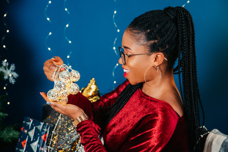 Young beautiful African American woman in red dress sitting and smiling on Christmas decorated backgroundの写真素材