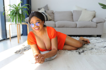 Cheerful young African American woman in orange dress smiling and playingの写真素材