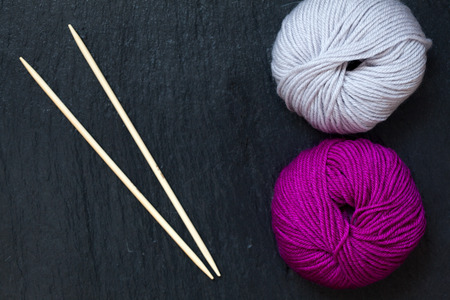 skein of pink and gray yarn with bamboo knitting needles with black slate backgroundの写真素材