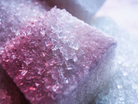 Heap of transparent white sugar crystals with large pieces of sugar in mixed colour light. Macro...