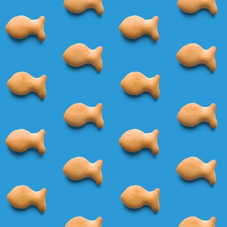 Rounded fresh crispy fish shaped cookies on light blue background. Seamless texture. Top viewの写真素材